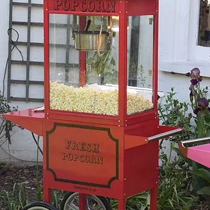 Our Popcorn machine with freshly popped popcorn, positioned on our red stand, outside ready for action.