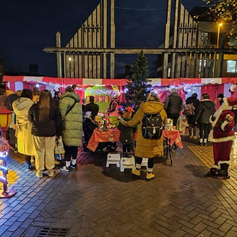 A crowded brick street with a row of bright red and white Christmas Carnival Side Stalls and lots of festive decorations at Christmas Market Event.