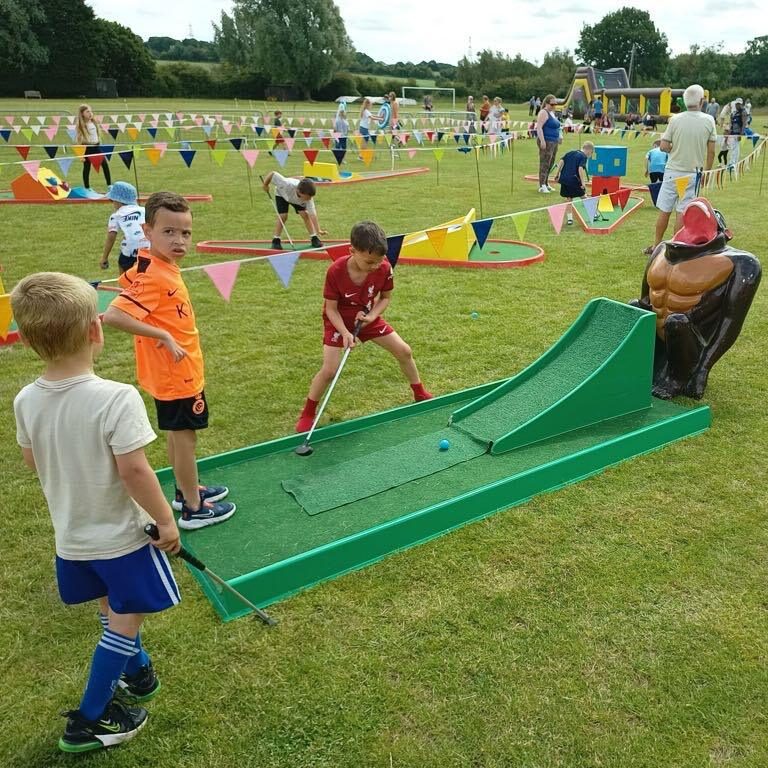 Our infamous Gorilla Golf Putt Challenge with Crazy Golf in the background, decorated with brightly coloured bunting and happy, focused children playing.