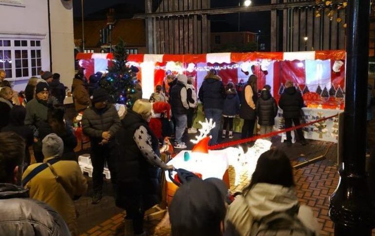 A crowded brick street with a row of bright red and white Christmas Carnival Side Stalls and lots of festive decorations at Christmas Market Event.
