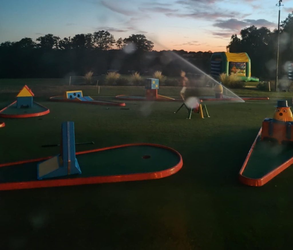 A beautiful photo of our 9 hole Crazy Golf and obstacles at dusk with the sprinklers turned on, all to welcome you to the Traditional Game Hire Company.