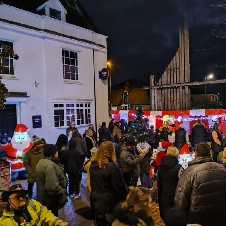 A crowded brick street with a row of bright red and white Christmas Carnival Side Stalls and lots of festive decorations at Christmas Market Event.